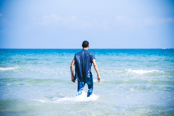 young muscular man resting and posing on the beach. A young man walks by the sea