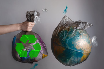 A woman's hand holds a garbage bag next to the globe of planet Earth. Concept of ecology and...