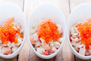 Fototapeta na wymiar Salad with seafood and red caviar in portioned bowls on a wooden table, horizontal