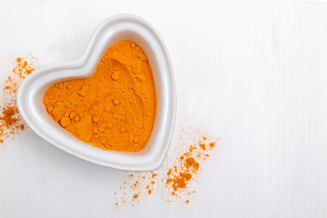 Bright yellow powder spice, turmeric or curry in a heart shaped bowl on the white table