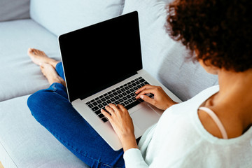 Over the shoulder view of woman sitting on couch and using laptop