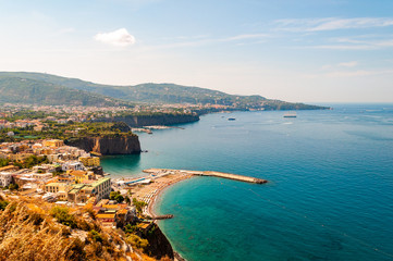 Fototapeta premium Panorama of high cliffs, Tyrrhenian sea bay with pure azure water, floating boats and ships, pebble beaches, rocky surroundings of Meta, Sant'Agnello and Sorrento cities near Naples region