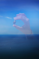 Fototapeta na wymiar Silhouette of a hand holding a shell on a background of the sea and a sailboat