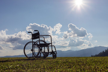 Empty wheelchair on the mountain meadow at sunset.