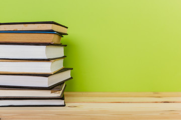 Simple composition of many hardback books, raw of books on wooden table and light green background