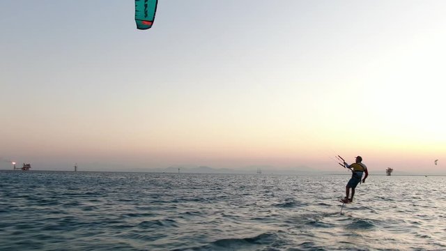 A man is using foil kiteboard, gliding in the sea above the water, sunset