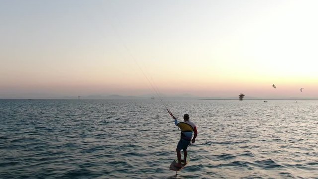 Aerial footage of a man kitesurfing on a foil kiteboard, gliding above the water