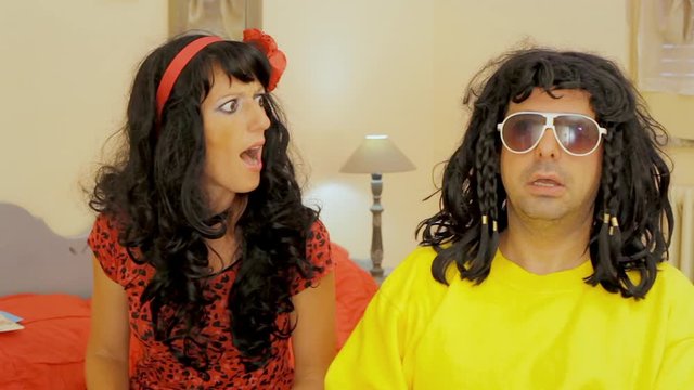 A very odd bizarre couple, a stoned man and a talkative woman, looking at the camera from their bedroom. Colorful weird people.