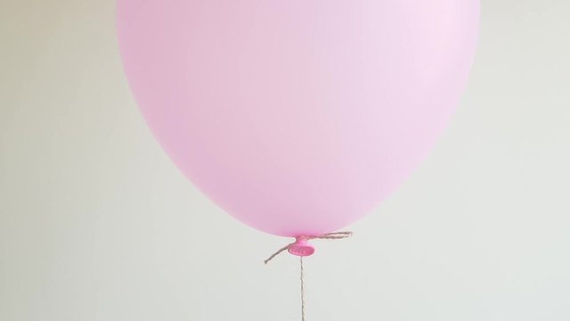 Light helium balloon in pink floating against off white wall, celebration, birthday concept