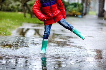 Close-up of kid wearing yellow rain boots and walking during sleet, rain and snow on cold day....