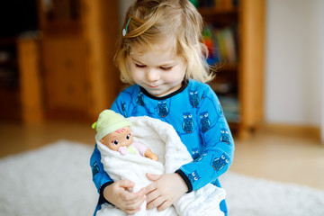 Adorable cute little toddler girl playing with doll. Happy healthy baby child having fun with role...