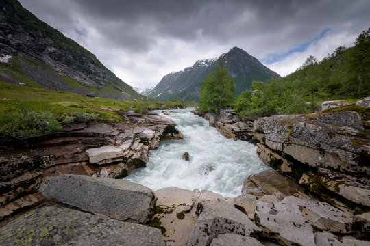 Norwegian green mountain scenery with glacial fed river raging down