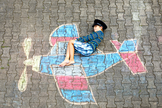 Little kid boy having fun with with airplane picture drawing with colorful chalks on asphalt. Child painting with chalk and crayon and going on vacations or dreaming of pilot profession.