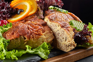 Stuffed fish on a wooden board, with herbs and vegetables, against a dark background