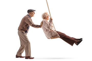 Senior man pushing his wife on a swing - obrazy, fototapety, plakaty