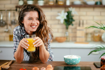 Young woman in kitchen. Beautiful woman in modern kitchen drinking orange juice.  - obrazy, fototapety, plakaty