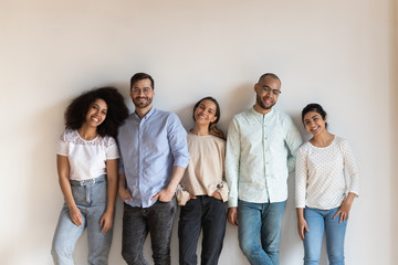 Smiling mixed race young friendly people standing near white wall.