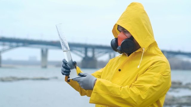 ecologist expert in a respirator Carefully examines the contents of the test tube and shows a gesture OK. Analysis of water from the river. Shakes to determine contamination. Ecology is modern.