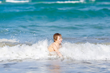 Adorable little blond kid boy having fun on ocean beach. Excited child playing with waves, swimming, splashing and happy about family vacations in Miami, Florida, USA..