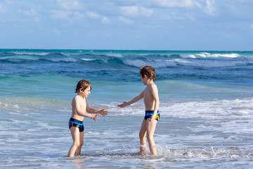 Two happy little kids boys running on the beach of ocean. Funny cute children, siblings, twins and best friends making vacations and enjoying summer day. Having fun with jumping into wave.