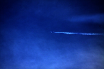 plane with condensation trail on dark blue sky