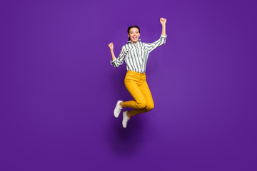Yeah. Full length photo of crazy pretty lady jumping high celebrating victory raising fists sports fan wear striped shirt yellow trousers isolated purple color background