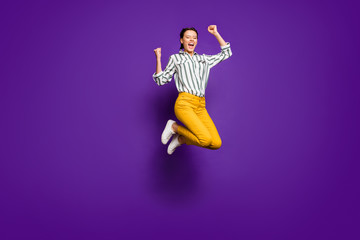 Full size photo of crazy pretty lady jumping high competitive sportswoman celebrating victory raising fists wear striped shirt yellow trousers isolated purple color background