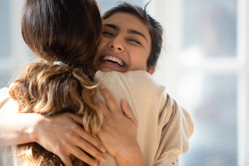 Happy mixed race girl cuddling smiling indian female friend.