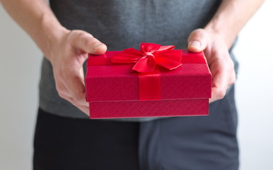 Midsection of man holding gift in red box with bow