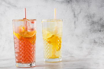 Two glass with lemonade and orange cocktail with lemon and orange, cold refreshing drink or beverage with ice on bright marble background. copy space. Advertising for cafe menu. Horizontal photo.