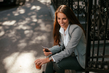 Beautiful businesswoman on coffee break using phone. Young businesswoman outdoors. 