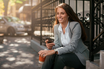 Beautiful businesswoman on coffee break using phone. Young businesswoman outdoors. 
