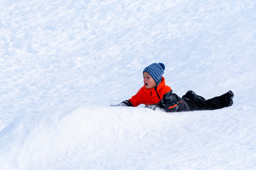 Fototapeta na wymiar Boy sledding down the hills without sledge on a winter day.