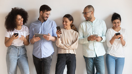 Happy diverse young people using different electronic devices.