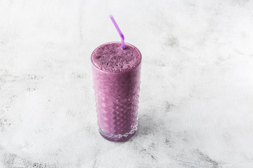 Blueberry smoothie or black currant purple milkshake in glass on bright marble background. Overhead...