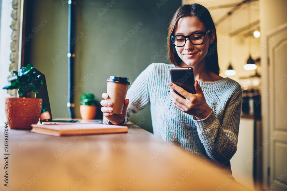 Poster cheerful hipster blogger with coffee to go in hands reading incoming sms message on smartphone conne