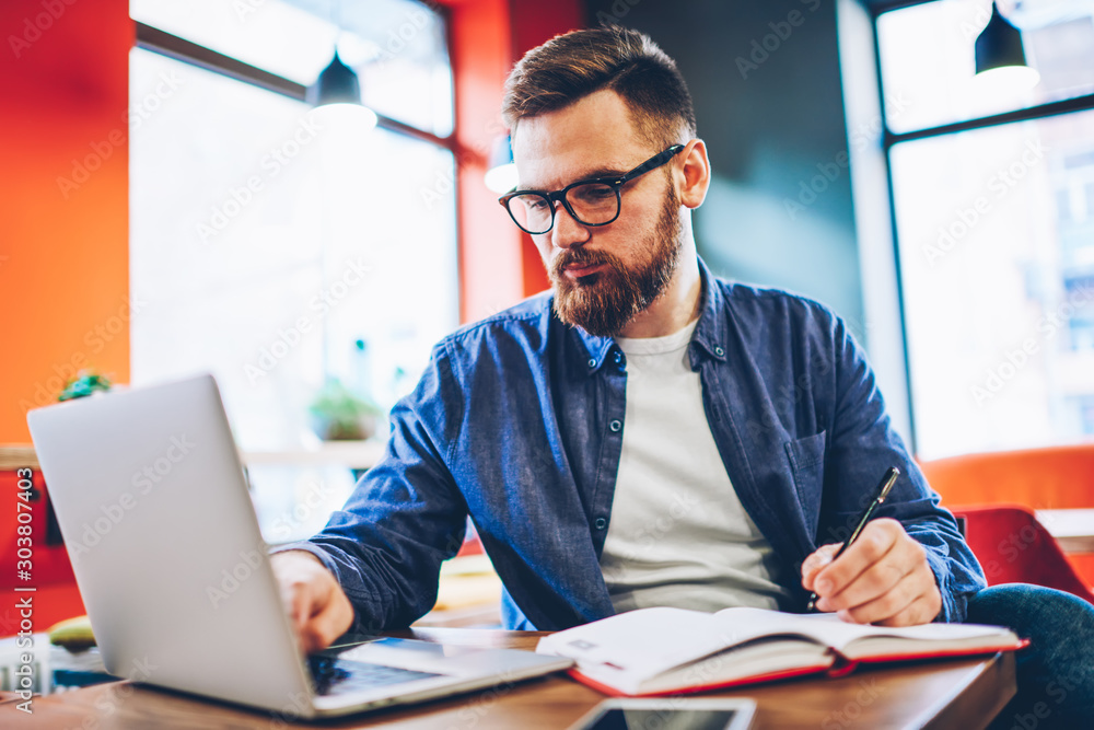 Poster creative male graphic designer drawing sketch in notepad while checking mail on modern laptop comput