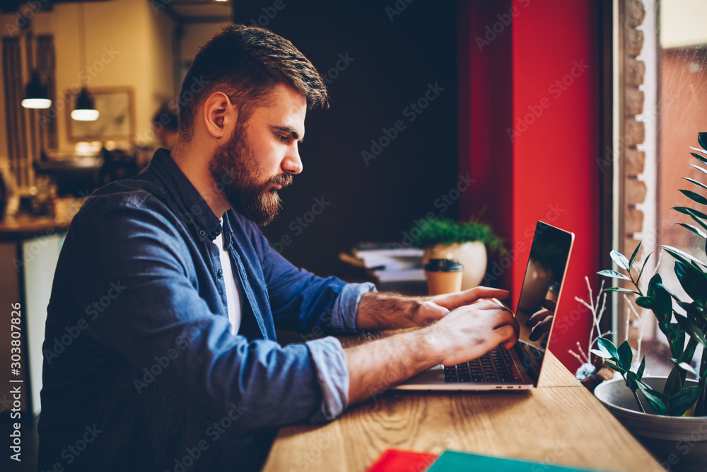Aufkleber side view of bearded freelancer keyboarding text information on modern laptop computer connected to 