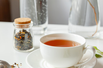 Obraz na płótnie Canvas Cup of hot black tea on white table with dry tea jar