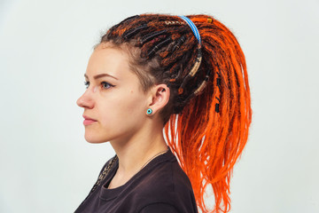 A girl with fiery red dreadlocks gathered in a ponytail on a white background side view. A young...