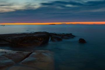 Sunset sky over stones and flat rock sinking under Baltic sea. Amazing wilderness of Estonia.