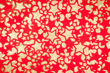 Festive holiday background of red construction paper with star cutouts on crinkly gold background