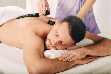 Fototapeta na wymiar Professional massage therapist massaging client back with hot stones. Alternative therapy, hot stone treatment