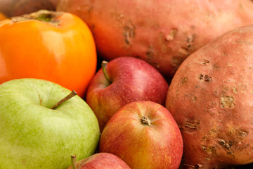 Colorful background with healthy fruits and vegetables like apples, kaki and sweet potatoes lying close together.