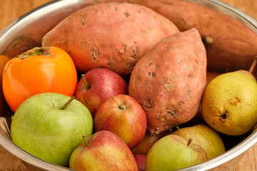 Colorful background with healthy fruits and vegetables like apples, kaki and sweet potatoes lying close together in a silver tin bowl.