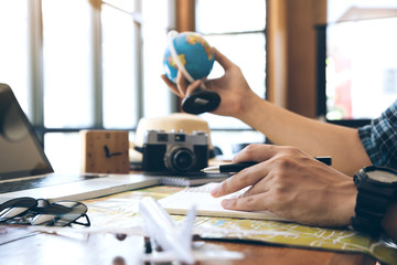 Male hand holding pen on notebook over map and other hand hold the globe. Planning a trip,copy space. Travel background