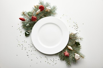 Top view of festive Christmas table setting on white background with decorated pine branch, plate...