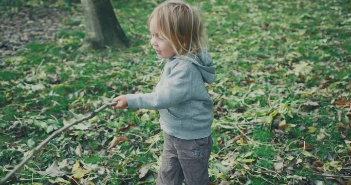 Little toddler playing with a stick in a park