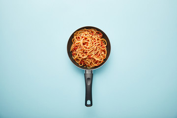 top view of delicious spaghetti with tomato sauce in frying pan on blue background