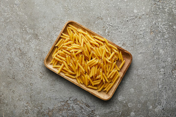 top view of raw penne on wooden board on grey textured surface